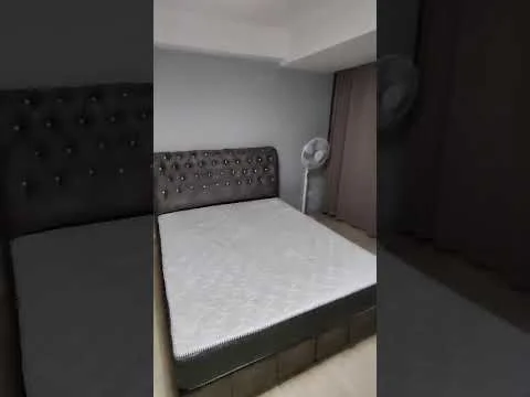 Bedroom features: king-size bed, upholstered headboard with tufted design, grey painted walls, light wood flooring, floor-to-ceiling curtains, ceiling fan, decorative wall, nightstand, window with natural light; style: modern.