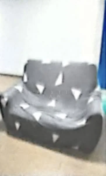 Living features: 2-seater fabric sofa in grey with triangular pattern, light-colored flooring, plain white walls, blue curtains.