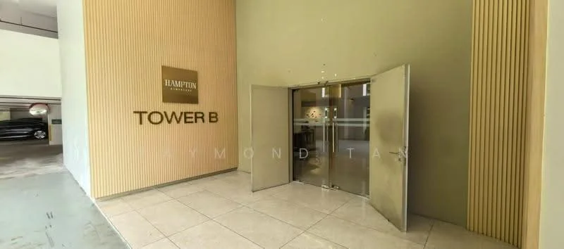 Exterior type: high-rise condominium; features: double-volume main lobby, glass entrance doors, cream painted facade, vertical wood paneling, marble flooring at entrance, signage for 'TOWER B', parking area visible, surrounded by greenery; style: modern.