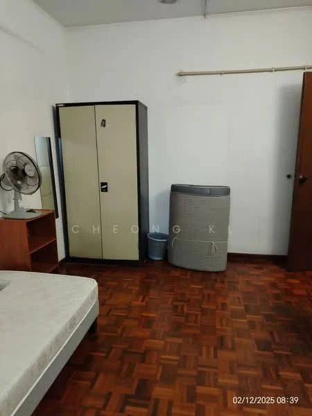 Room features: wooden flooring, white walls, single wardrobe with two-tone finish, brown wooden bedside table, circular ceiling fan, grey air conditioning unit, blue waste bin.