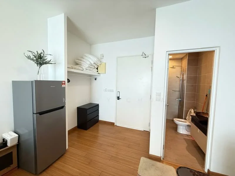 Room features: grey fridge, black dresser, white walls, wooden flooring, bathroom door, shower area visible, toilet visible, bed with pillows on top; style: modern.
