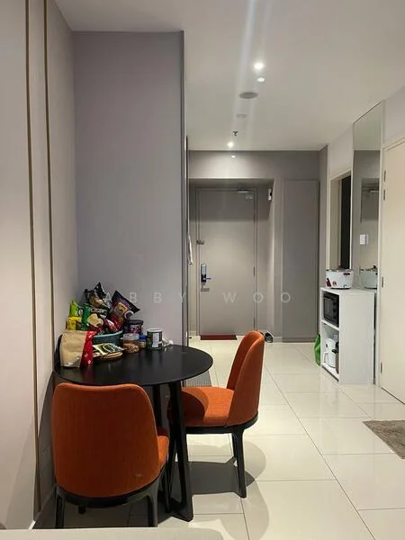 Dining features: round black dining table, 2 orange upholstered dining chairs, white tiled flooring, grey painted walls, recessed downlights, wall-mounted mirror, open doorway to hallway, microwave on countertop, snack items on table; style: modern. Hallway features: white tiled flooring, grey painted walls, open doorway to main entrance, built-in cabinets, door to bathroom, door to bedroom.