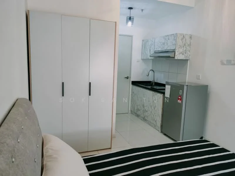 Room features: queen-size bed with upholstered headboard, striped bedding, white wardrobe with black handles, kitchenette with marble countertop, stainless-steel sink, chrome pull-down faucet, built-in kitchen cabinets, stainless-steel fridge, white tiled flooring, recessed ceiling lights, wall-mounted light fixture; style: modern.