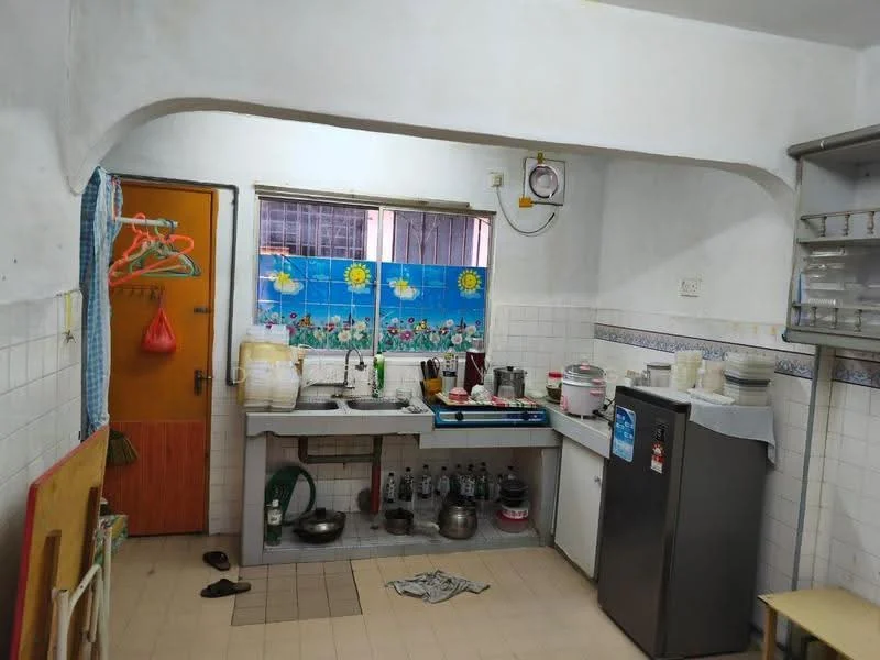 Kitchen features: white painted walls, tile flooring, single-bowl stainless-steel sink, chrome pull-down faucet, gas stove with 4 burners, built-in kitchen cabinets, refrigerator, window with floral curtain, countertop, wall-mounted clock, kitchen utensils visible, floor space with shoes.