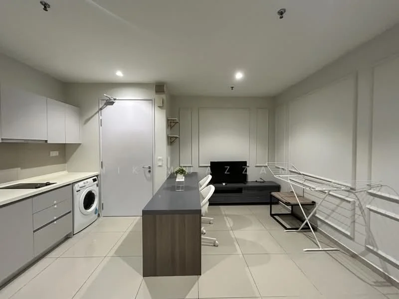 Room features: white cabinets, grey countertop, built-in washing machine, freestanding TV cabinet, black TV, folding drying rack, tile flooring, recessed lighting, white walls, open shelving, 3 white chairs, kitchen island; style: modern.