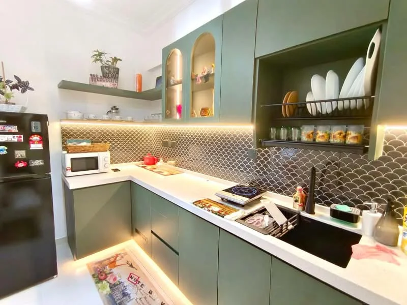 Kitchen features: green cabinetry, white countertop, black sink, stainless-steel faucet, built-in microwave, black fridge, ceramic cooktop, decorative backsplash with fish scale pattern, open shelving, under-cabinet lighting, kitchen rug with colorful design, various kitchen utensils and decor; style: modern.