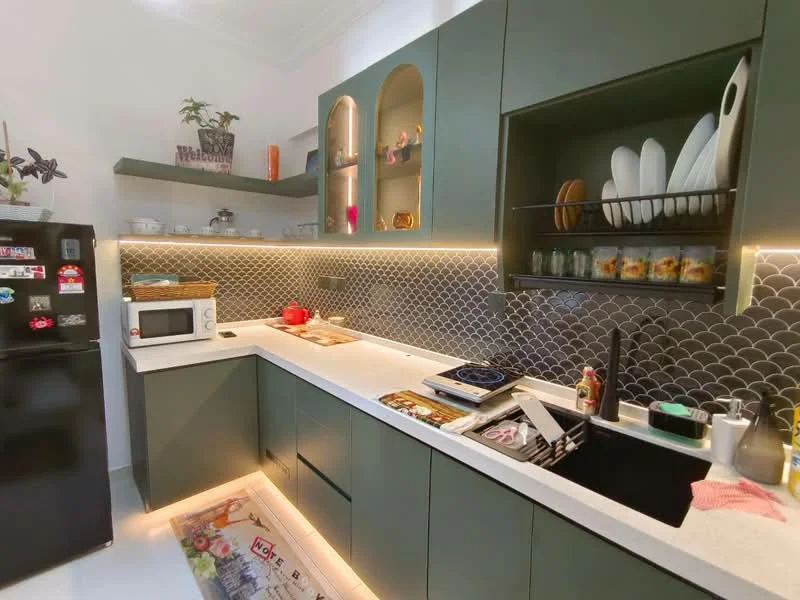 Kitchen features: green cabinetry, white quartz countertop, black single-bowl stainless-steel sink, chrome pull-down faucet, microwave, stainless-steel fridge, black cooktop, grey mosaic tile backsplash, under-cabinet LED lighting, open shelving, decorative plants, kitchen utensils, dishware, area rug with colorful design; style: modern.