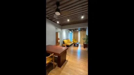 Living features: wooden flooring, grey painted walls, exposed wooden ceiling beams, 5-blade ceiling fan, large windows with sheer curtains, yellow fabric sofa, wooden dining table, wooden dining chairs, potted plant, area rug; style: modern.