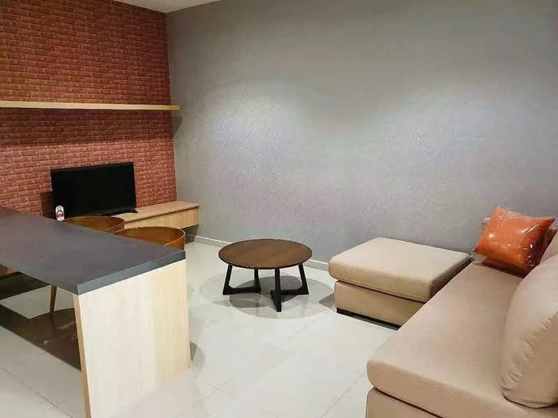 Living features: exposed brick accent wall, grey painted walls, light-colored tiled flooring, L-shape sectional sofa in beige, orange decorative pillow, round coffee table with black legs, TV console with wooden finish, wall-mounted TV, open shelving above TV console, dining table with wooden finish, two wooden dining chairs; style: modern.