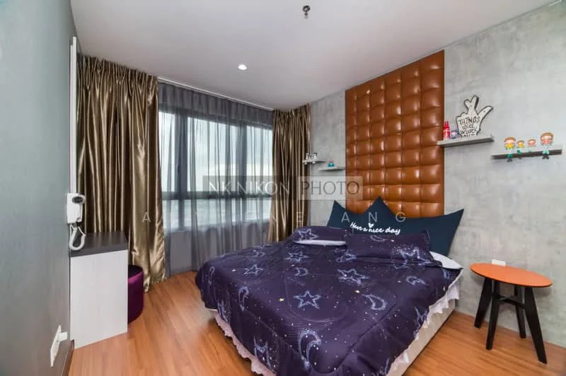 Bedroom features: queen-size bed with dark blue bedding featuring stars, upholstered headboard in brown, wooden flooring, grey painted walls, floor-to-ceiling window with sheer curtains, decorative wall with textured panels, small round side table in orange, wall-mounted phone, decorative figurines on shelf, curtains in gold, wall-mounted light fixture; style: modern; view: city.
