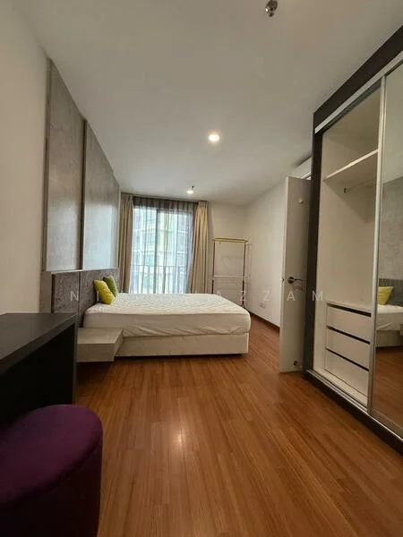 Bedroom features: queen-size bed with white bedding, upholstered headboard, built-in wardrobe with sliding mirror doors, wooden flooring, floor-to-ceiling windows, sheer curtains, wall-mounted light fixture, decorative wall paneling, study desk, purple ottoman; style: modern.