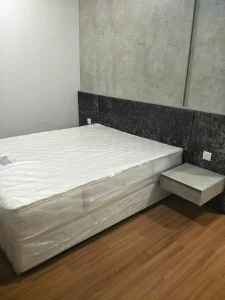Bedroom features: queen-size bed, grey upholstered headboard, wooden flooring, concrete accent wall, nightstand with drawer, wall-mounted electrical outlets, minimalist decor; style: modern.