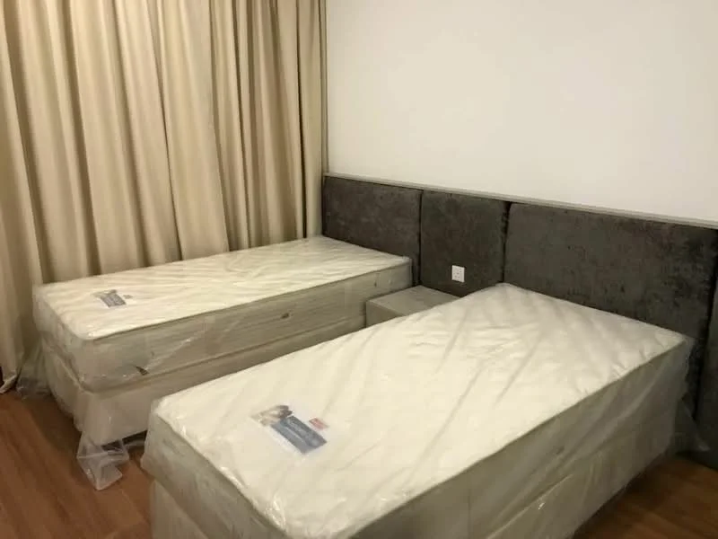 Bedroom features: two single beds with mattresses, upholstered headboard, wooden flooring, cream curtains, wall-mounted electrical outlet, neutral wall color; style: modern.