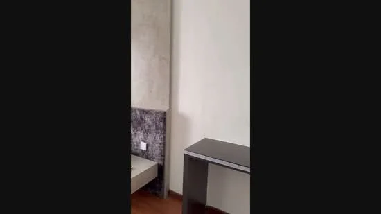 Room features: light wooden flooring, white painted walls, textured accent wall, small side table, bed frame without mattress, electrical outlets visible; style: modern.