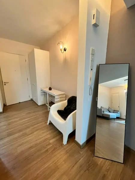 Room features: wooden flooring, white walls, wall-mounted light fixture, full-length mirror, white chair, small desk, intercom panel, doorbell, closet, decorative item on desk; style: modern.