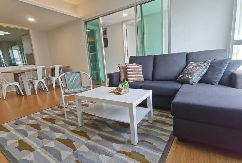 Living features: L-shape sectional sofa in dark grey, coffee table with white finish, area rug with geometric pattern, decorative cushions, wooden flooring, floor-to-ceiling windows, wall-mounted light fixture, open layout to dining area; style: modern. Dining features: 6-seater dining table, metal dining chairs, open layout to living area; style: modern.