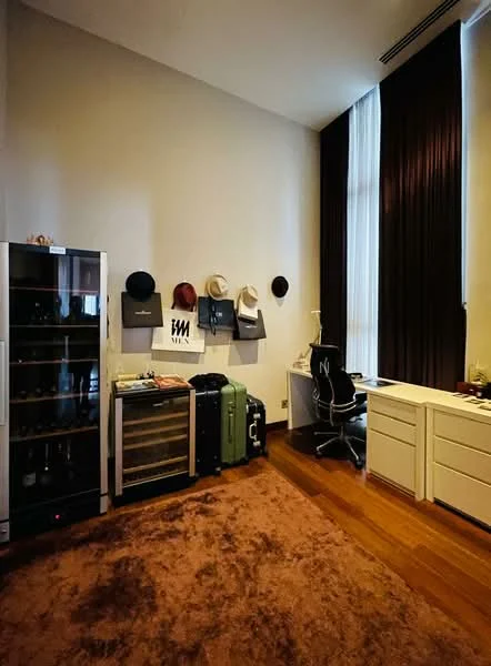 Study features: wooden flooring, cream painted walls, floor-to-ceiling windows with sheer curtains, desk with chair, white cabinetry, wine fridge, wine rack, suitcases, hats displayed on wall, area rug with brown color; style: modern.