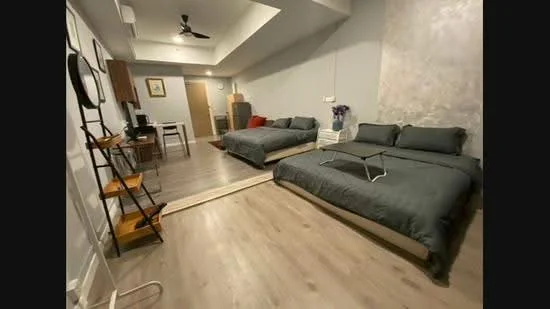 Bedroom features: two queen-size beds with grey bedding, wooden flooring, grey painted walls, exposed concrete accent wall, ceiling fan, recessed lighting, nightstand with lamp, study desk with chair, wall-mounted mirror, decorative wall art, open shelving unit, window with sheer curtains; style: modern.