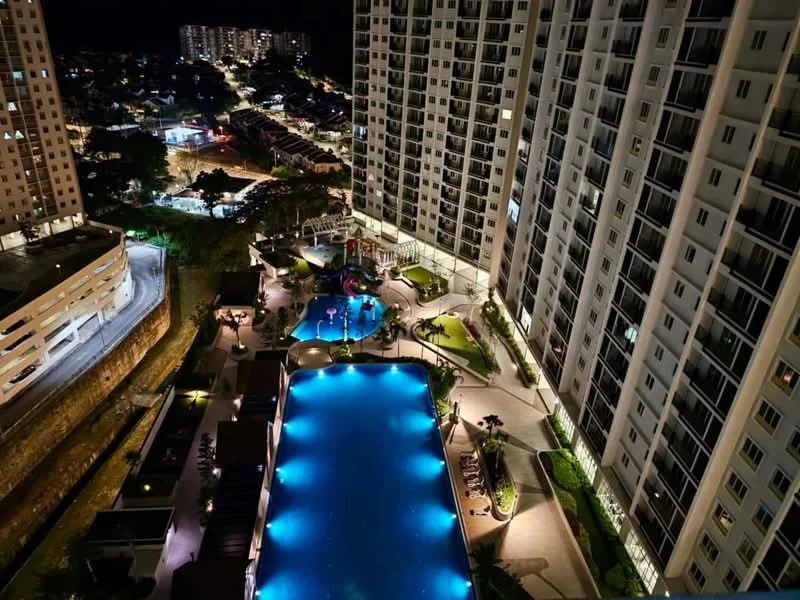 Exterior type: high-rise condominium; features: infinity pool, pool deck with loungers, landscaped garden, children's playground, water features, night lighting, surrounding residential buildings, manicured pathways; style: modern.