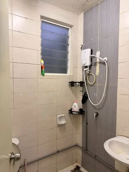 Bathroom features: white tiled walls, grey accent wall, shower with wall-mounted showerhead, toilet, small window with horizontal slats, soap dispenser, shower caddy, exposed plumbing, floor drainage.