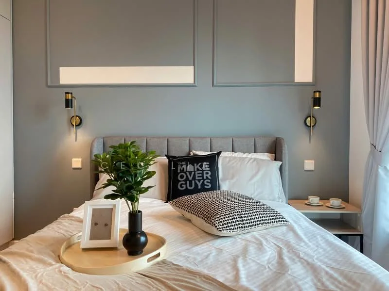 Bedroom features: queen-size bed with grey upholstered headboard, white bedding, black and white decorative pillows, bedside table with two cups, decorative tray with plant, wall-mounted sconces, grey painted walls, curtains, framed artwork, geometric patterned cushion; style: modern.