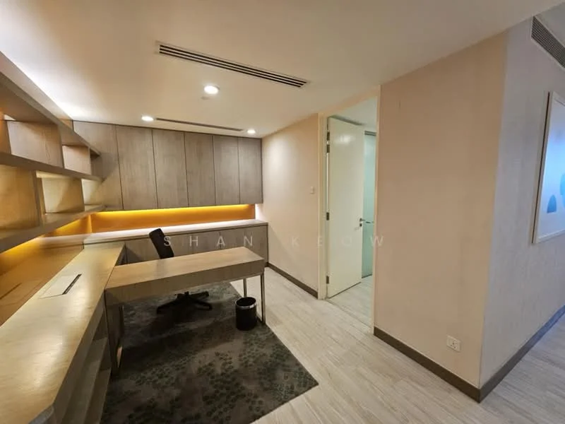 Study features: wooden desk, built-in cabinetry with warm lighting, light-colored walls, laminate flooring, recessed ceiling lights, door leading to hallway, decorative wall art, area rug with geometric pattern; style: modern.
