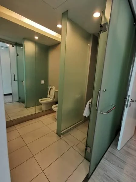 Bathroom features: glass shower enclosure, white toilet, light grey tiled flooring, green glass partition, mirror wall, recessed lighting, white walls, sliding door; style: modern.