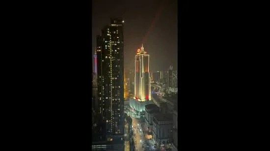 Exterior type: high-rise condominium; features: illuminated facade, glass curtain wall, surrounded by city skyline, night lighting, tall structure, nearby high-rise buildings, street view, urban context; style: modern.
