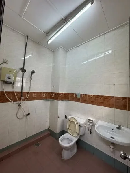 Bathroom features: white tiled walls, brown accent tiles, grey tiled flooring, shower with handheld showerhead, toilet, wall-mounted sink, mirror above sink, overhead fluorescent lighting.