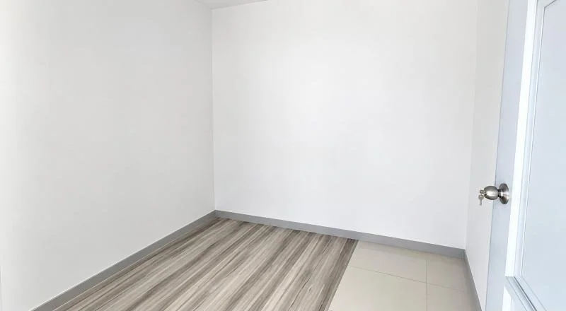 Room features: white painted walls, grey skirting boards, light wood-look vinyl plank flooring, cream ceramic tile flooring, plain white ceiling, single hinged door with frosted glass panel, chrome round door knob, minimalist unfurnished room; style: minimalist.