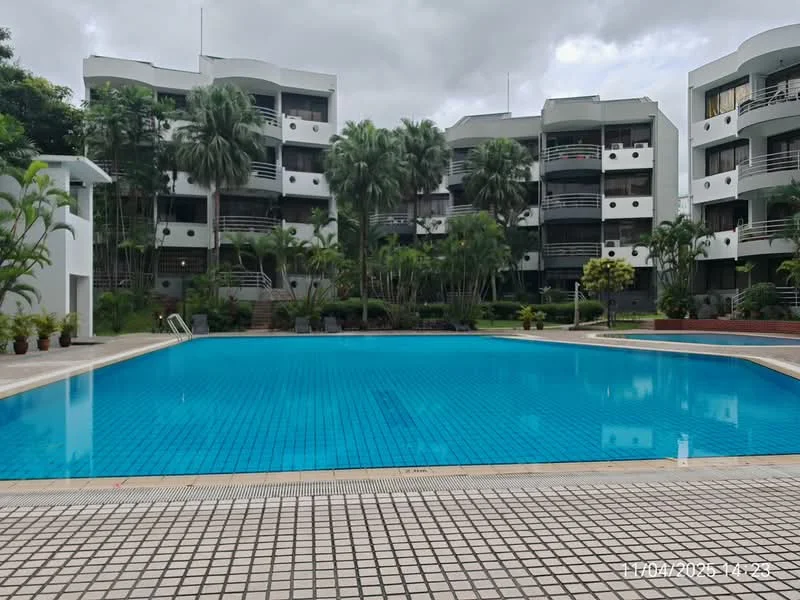 Exterior type: low-rise apartment block; features: swimming pool, pool deck with loungers, landscaped garden with palm trees, manicured lawn, multiple levels of apartments, balconies with glass railings, paved walkway around the pool; style: modern.