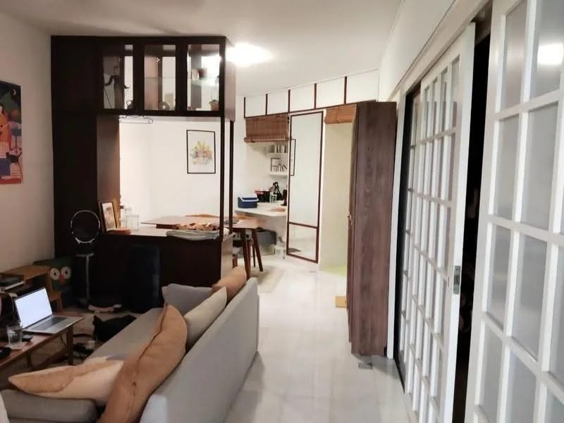 Living features: 3-seater fabric sofa in light beige, wooden coffee table, floor-to-ceiling windows with white frames, white painted walls, marble flooring, decorative wall art, built-in shelving unit, area rug with geometric pattern, laptop on a side table; style: modern. Kitchen features: open kitchen layout, wooden cabinetry, countertop with bar seating, kitchen island, stainless-steel appliances, white backsplash, hanging light fixtures; style: modern. Room features: glass panel doors, wooden door, neutral color scheme.