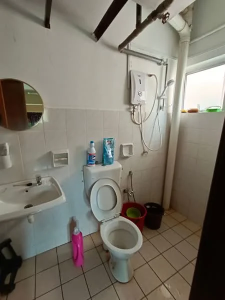 Bathroom features: white tiled walls, white tiled flooring, one-piece toilet, single-sink vanity with wall-mounted faucet, round mirror, shower with wall-mounted water heater, window for natural light, cleaning supplies visible, plastic storage bins, exposed plumbing, light fixture on ceiling.