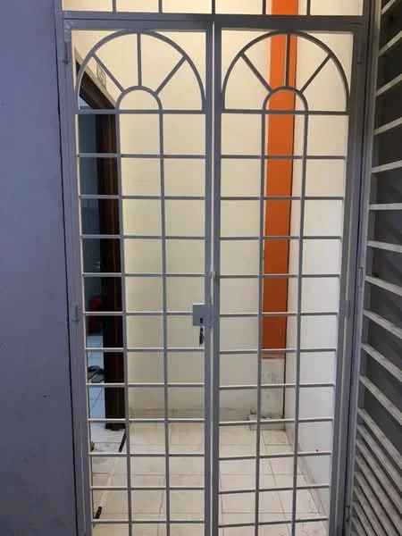 Room features: double metal security gate, white painted metal frame, grid pattern design, orange accent wall, white tiled flooring, doorway leading to another room, neutral wall color, visible floor area; style: modern.