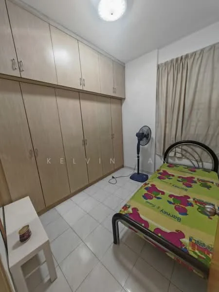 Bedroom features: single bed with black metal frame, colorful bedspread with cartoon characters, built-in wardrobe with wooden finish, white tiled flooring, curtains in light fabric, ceiling light fixture, standing fan, small white shelf unit.