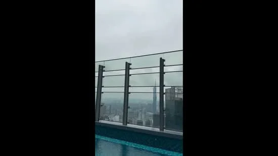 Exterior type: high-rise condominium; features: infinity pool, glass railing, city skyline view, water feature, tile pool deck, surrounding urban landscape; style: modern.
