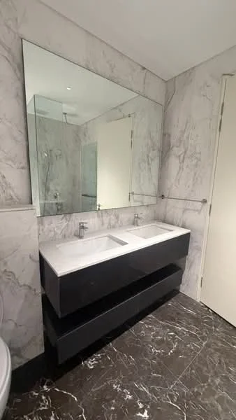 Bathroom features: double-sink vanity with marble top, black cabinetry, large wall mirror, marble wall cladding, marble flooring, glass shower enclosure, chrome basin mixers, white toilet, towel rail; style: modern.