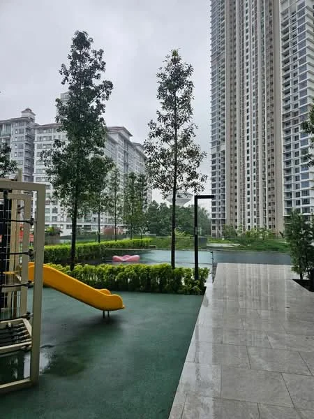 Exterior type: high-rise condominium; features: children's playground with slide, manicured landscaping, mature trees, swimming pool, pool deck, surrounding greenery, modern high-rise buildings, wet pavement, outdoor seating area; style: modern.