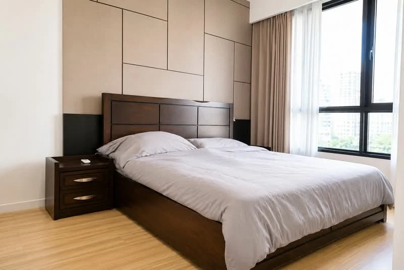 Bedroom features: king-size bed with grey bedding, wooden bed frame, nightstand with drawer, laminate flooring, large window with sheer curtains, accent wall with geometric pattern, light-colored walls, decorative wall paneling; style: modern; view: city.