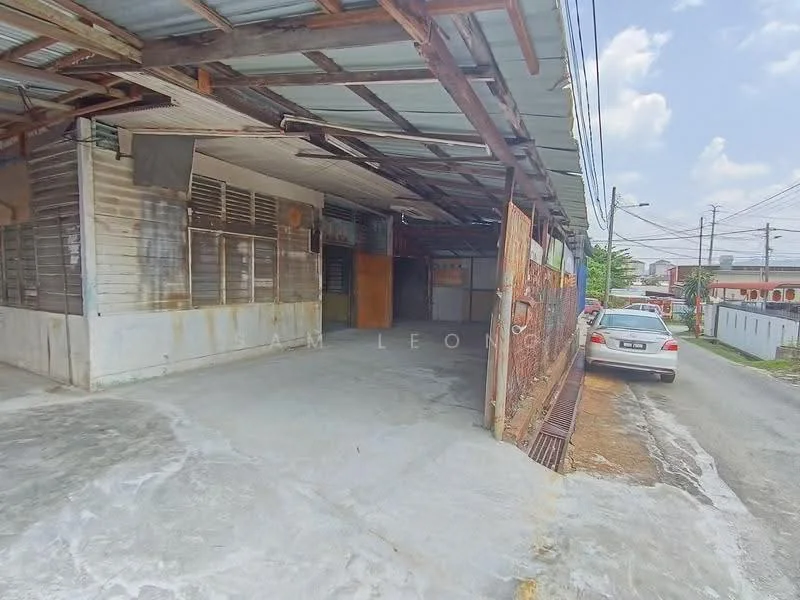 Exterior type: shophouse; features: metal roof, concrete flooring, exposed beams, open space, frontage with metal grilles, parking space for one car, surrounding concrete walls, partially covered area, utility poles visible, street view, nearby residential area; style: traditional.