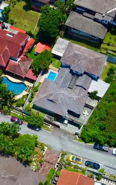 Exterior type: detached bungalow; features: flat roof, grey tiled roof, manicured lawn, swimming pool, outdoor patio area, surrounded by greenery, driveway with interlocking pavers, adjacent to residential street; style: modern.