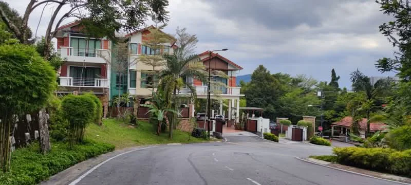 Exterior type: detached bungalow; features: multi-storey building, green landscaping with mature trees, manicured lawn, paved driveway, balconies on upper floors, gated entrance, surrounded by greenery, road access, modern facade with large windows, terracotta roof tiles; style: modern.