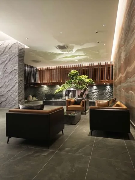 Room features: grey marble flooring, feature wall with stone cladding, wooden slatted wall, recessed LED downlights, indoor tree, two black leather sofas with brown cushions, coffee table, decorative planter, wall-mounted air conditioning unit, modern decor elements; style: modern.