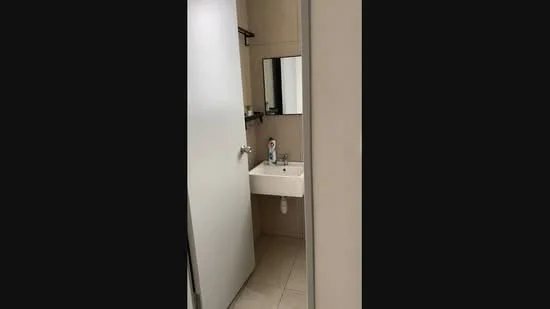 Bathroom features: white painted walls, tile flooring, single-bowl sink, chrome basin mixer faucet, mirror above sink, shelf above sink, door, light fixture, toilet, towel rack.