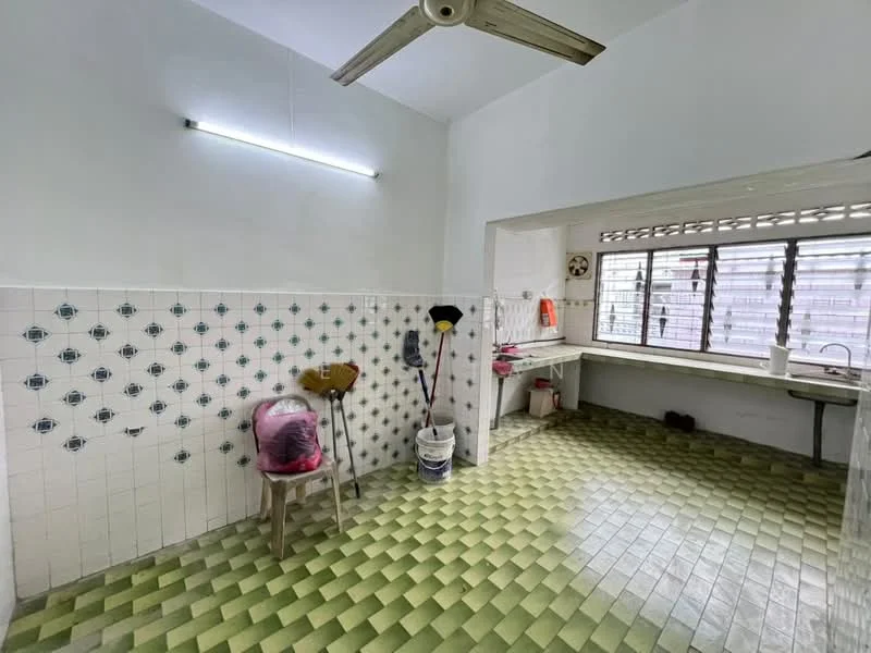 Kitchen features: green and yellow checkered tile flooring, white painted walls, wall-mounted fluorescent light, window with metal grille, sink with faucet, countertop, cleaning supplies visible, chair.