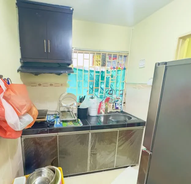 Kitchen features: black cabinetry, stainless-steel sink, chrome faucet, countertop with metallic finish, refrigerator, window with security bars, wall tiles with decorative border, floor tiles, various kitchen utensils, plastic bags, cleaning supplies.