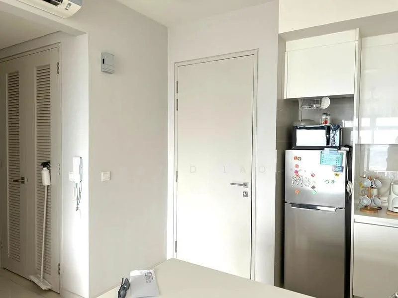 Room features: white painted walls, light grey flooring, built-in cabinets with louvered doors, white door, stainless-steel fridge, white countertop, kitchen appliances on countertop, wall-mounted air conditioning unit; style: modern.