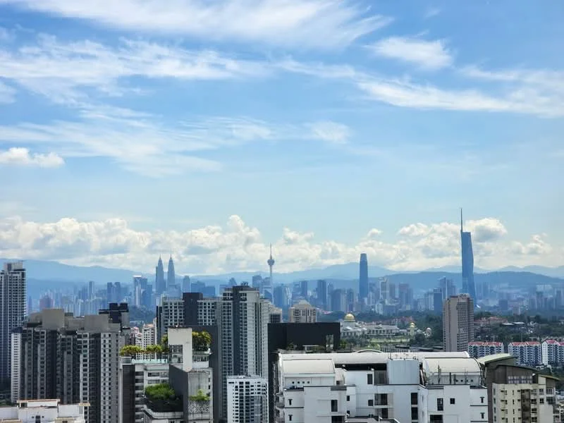 Exterior type: high-rise condominium; features: city skyline view, multiple high-rise buildings, green rooftops, urban landscape, clear blue sky, distant mountains, clouds in the sky; style: modern.