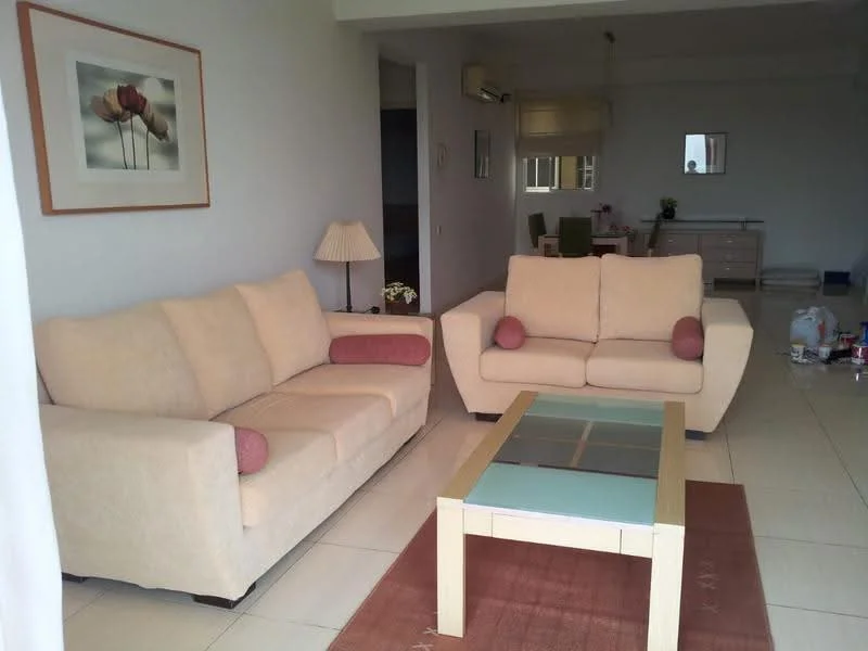 Living features: 2-seater fabric sofa in beige, 3-seater fabric sofa in beige, coffee table with glass top, area rug with geometric pattern, wall-mounted air conditioning unit, framed artwork on wall, lampshade table lamp, tile flooring; style: modern.