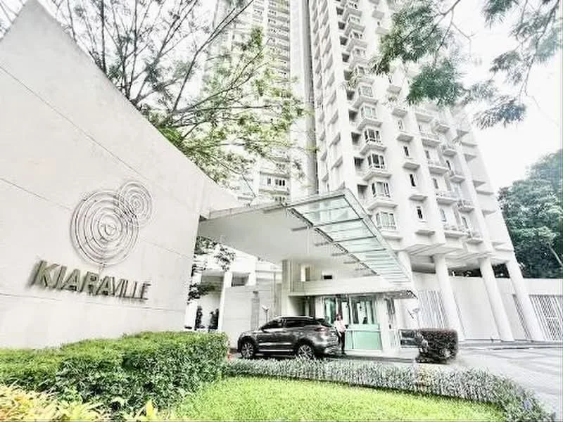 Exterior type: high-rise condominium; features: modern facade with glass elements, covered entrance with glass canopy, landscaped garden with manicured lawn, signage with 'Kiaraville', parking area visible, surrounded by greenery, multiple storeys visible, security entrance with guard house; style: modern.